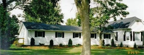 Single-story white Regency at Troy facility with front lawn, trees, and shrubs.