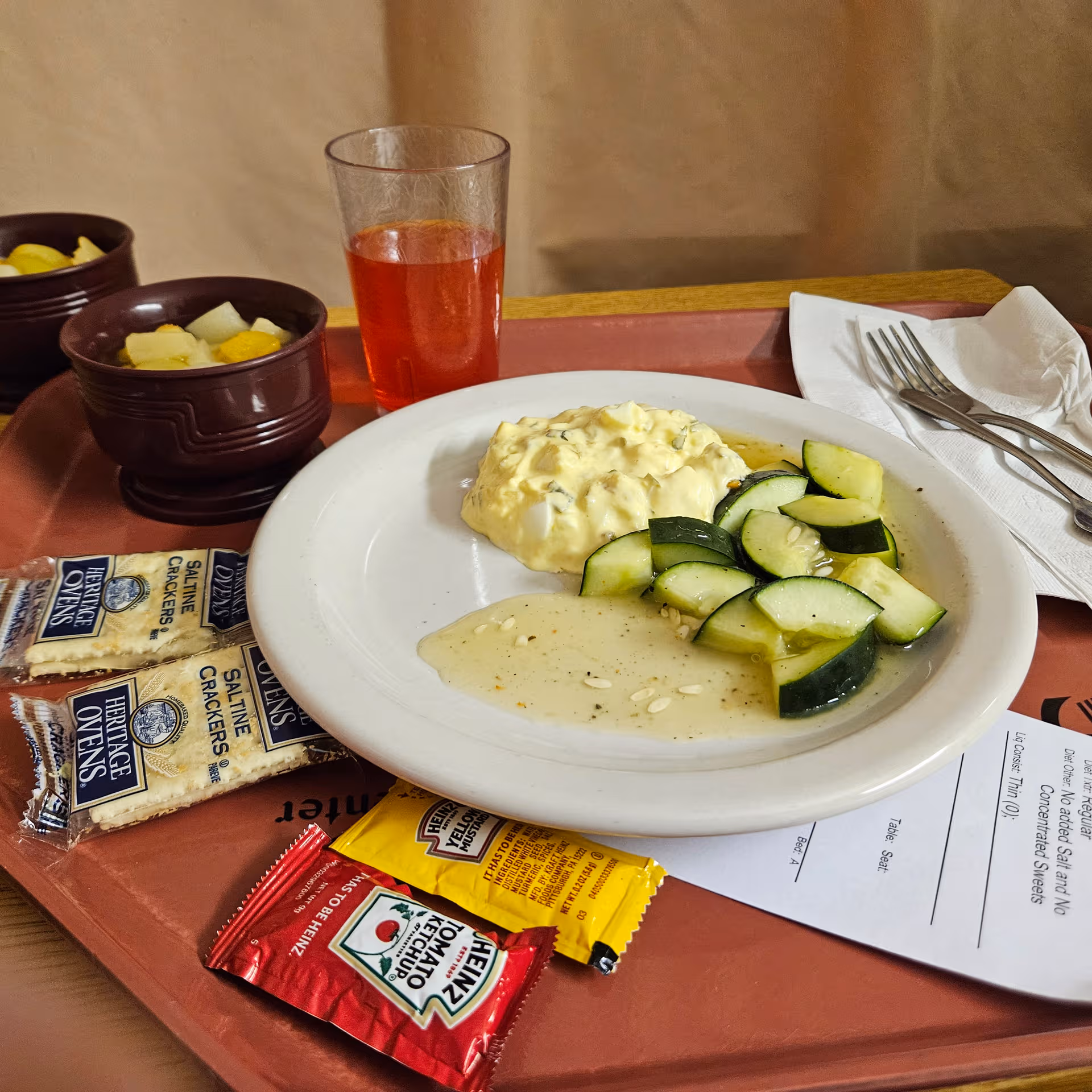 Meal on a red tray with cucumber slices, potato salad, juice, and snack packets.