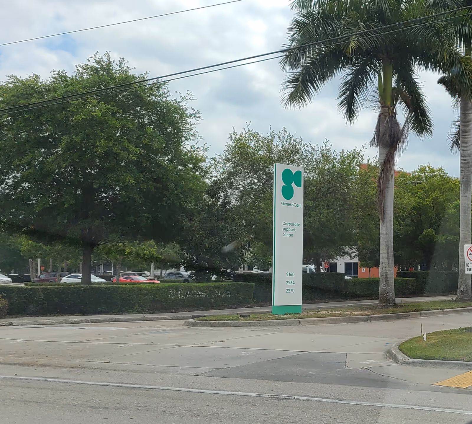 Exterior view of a GenesisCare sign beside a road with trees and cars