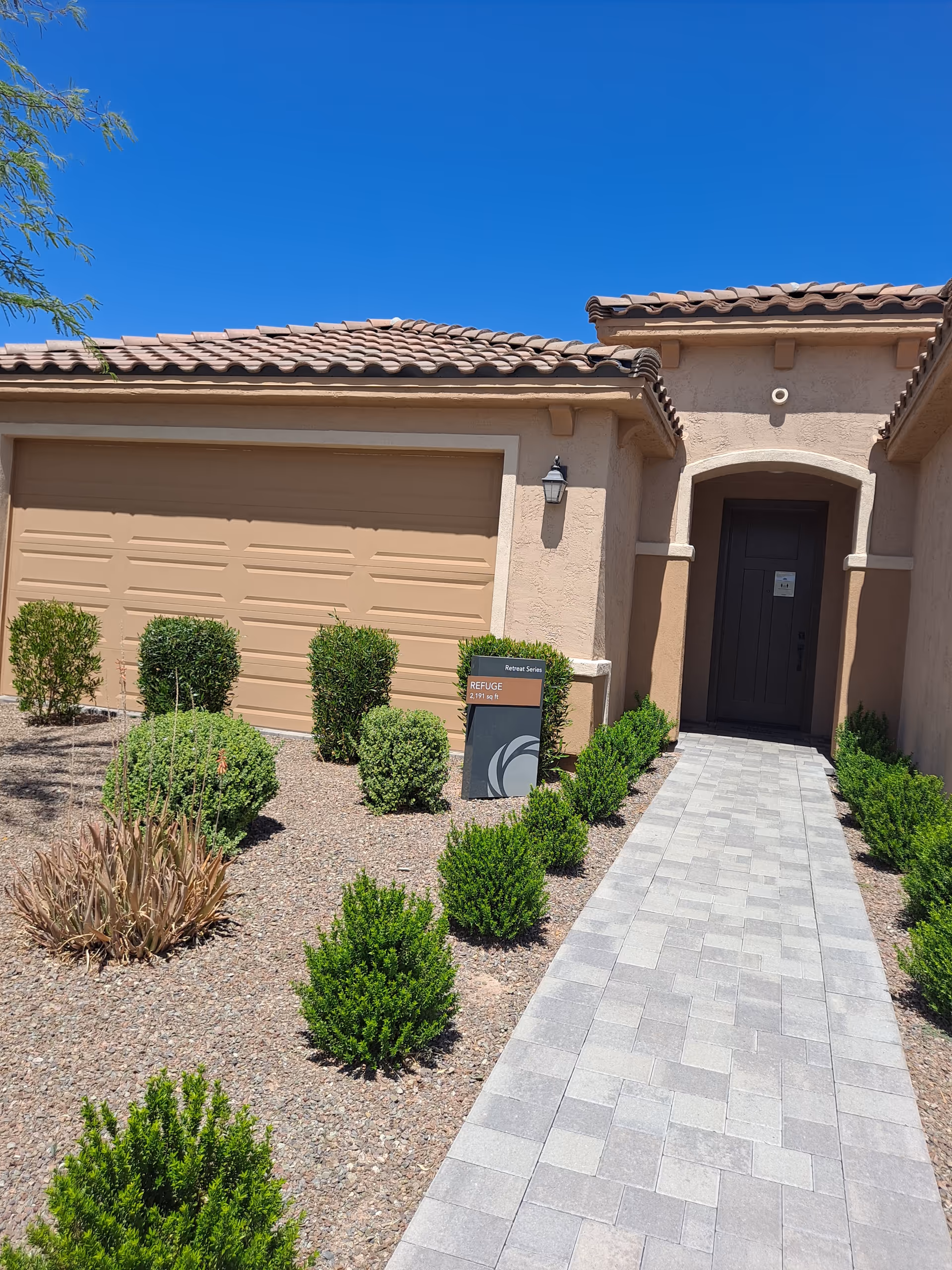 Desert landscaping frames a beige senior living building with a paved walkway to a front door