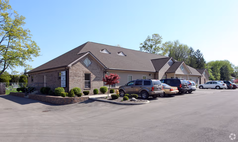 Exterior view of a brick senior living facility with a parking lot and cars