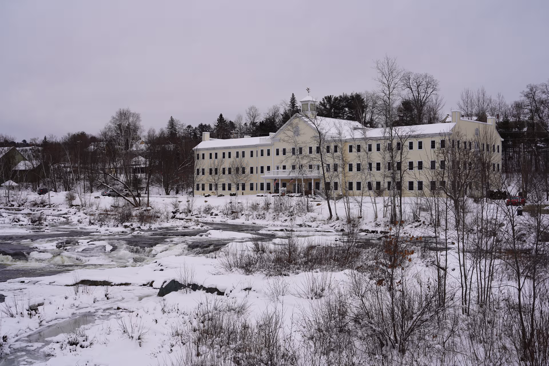 Riverglen House exterior shows a large beige building beside a snowy river in winter.