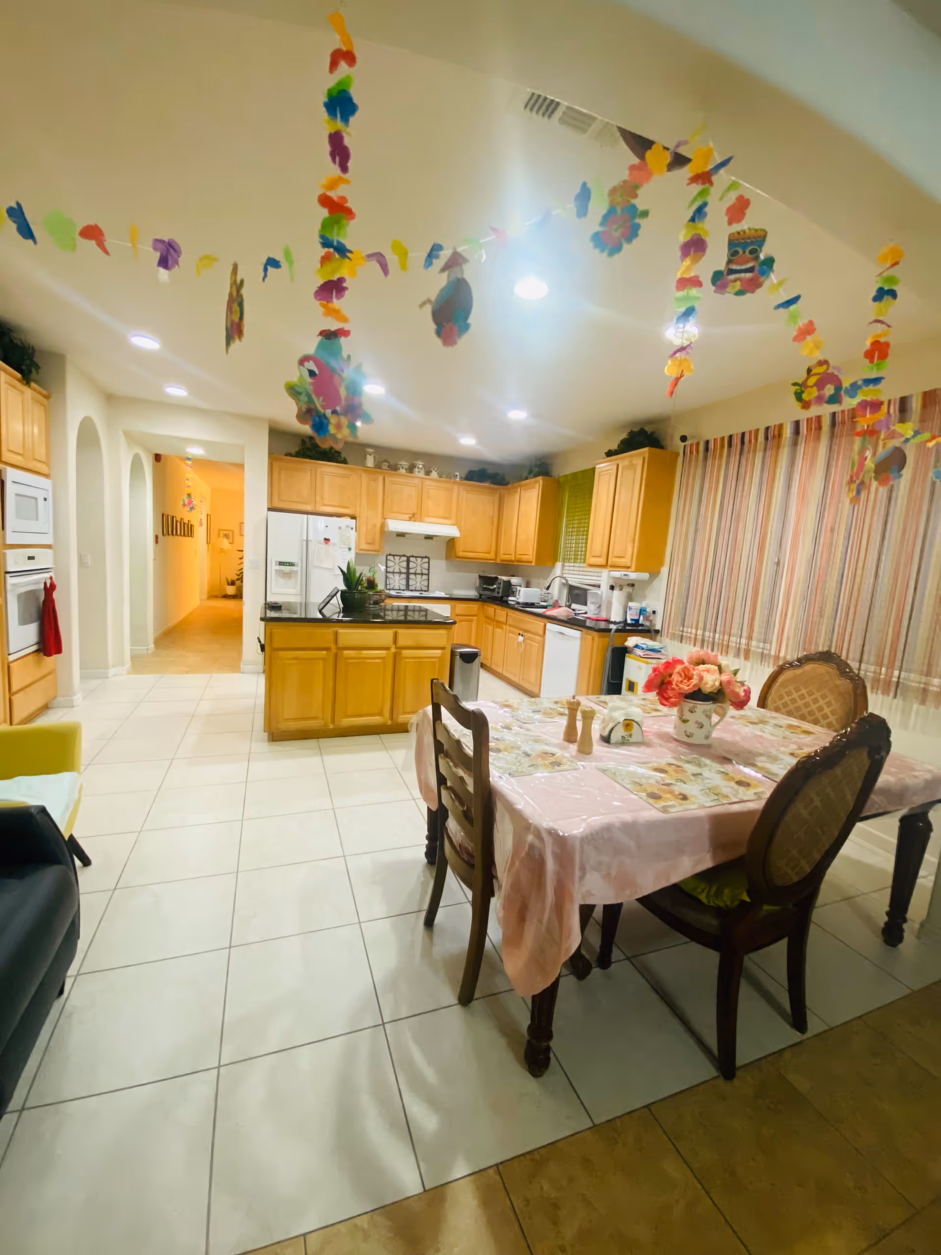 Bright communal kitchen and dining area with colorful ceiling decorations and a pink tablecloth.