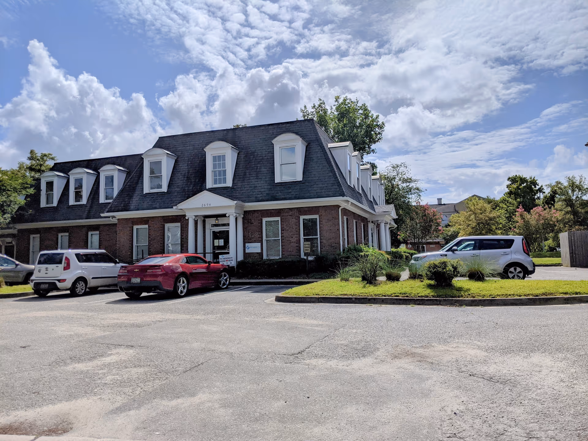 Two-story brick senior living facility with dormer windows and a parking lot in front.