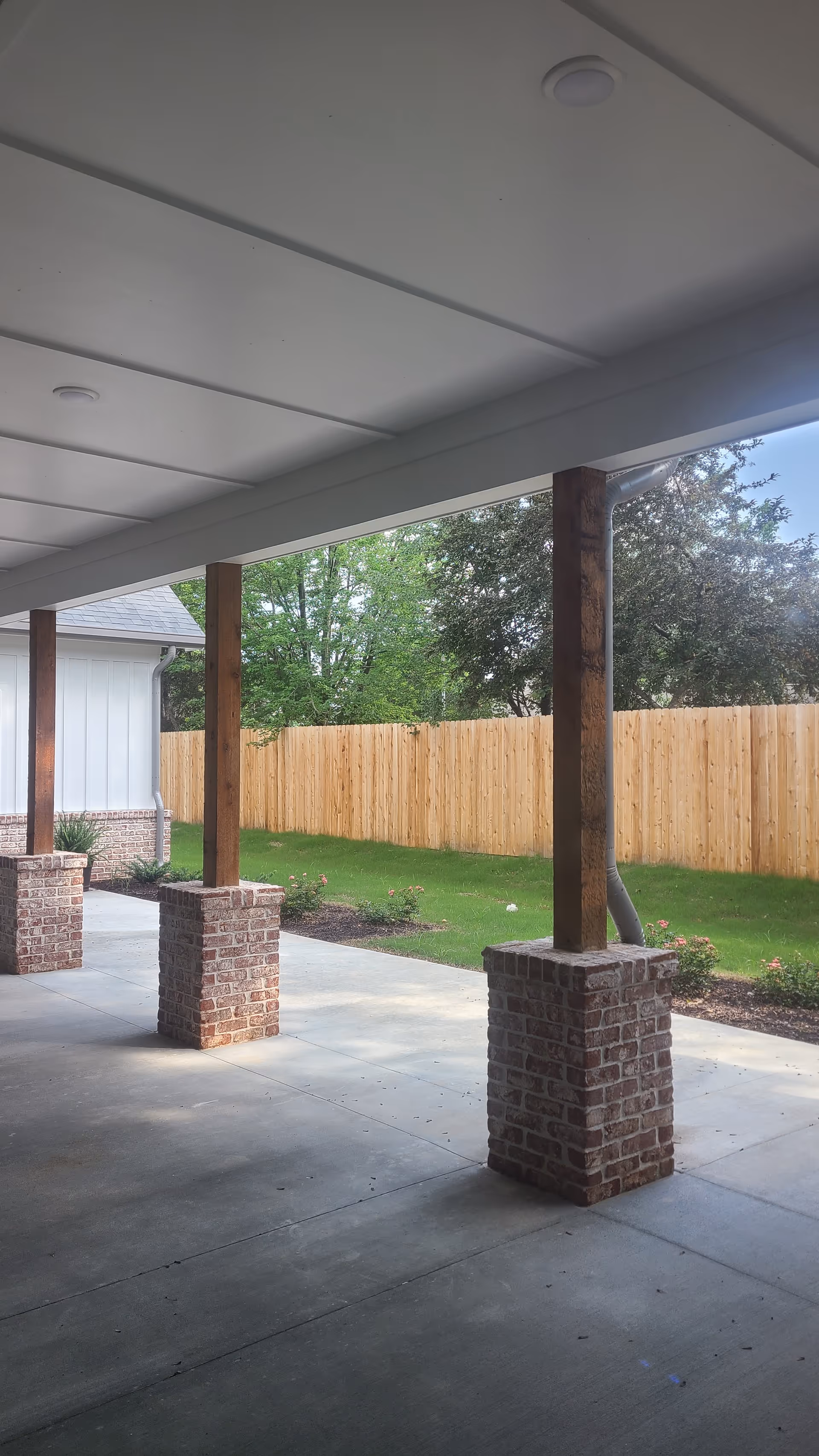Covered outdoor walkway with brick columns, wooden posts, and a green lawn.