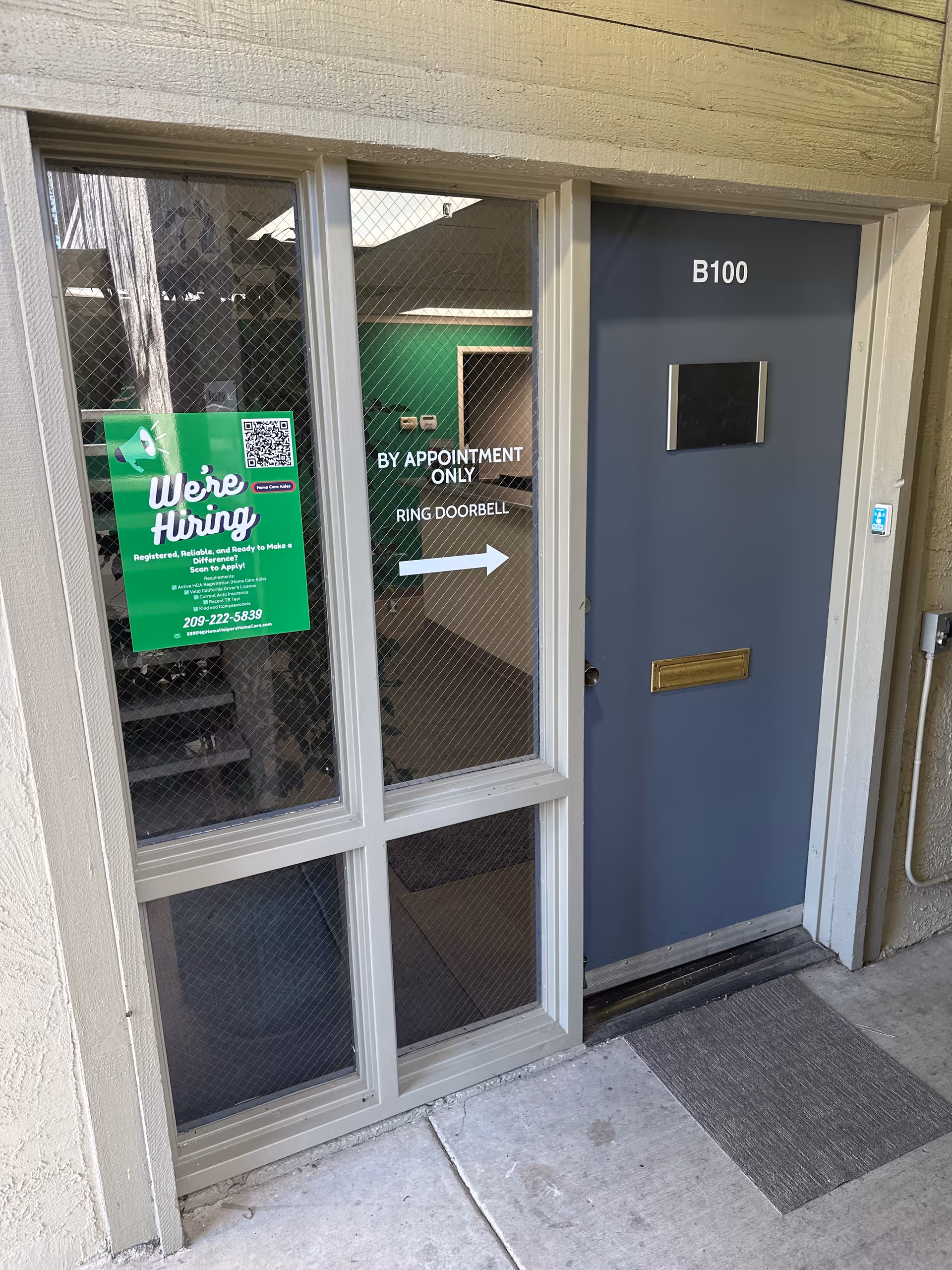 Exterior building entrance with B100 door, glass panels, and a We're Hiring sign.