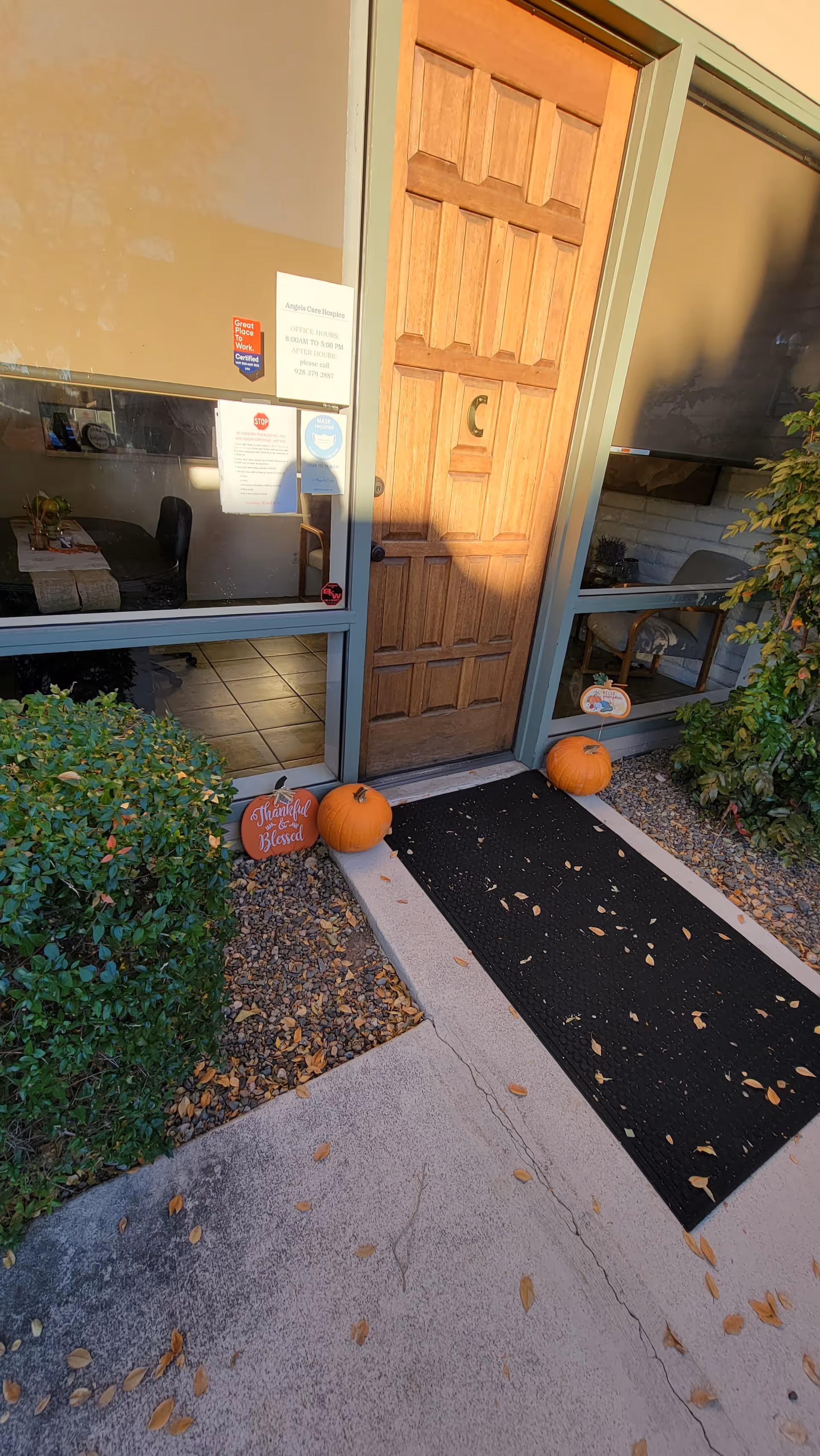 Entrance to Angels Care Hospice with pumpkins, a wooden door, and glass windows.