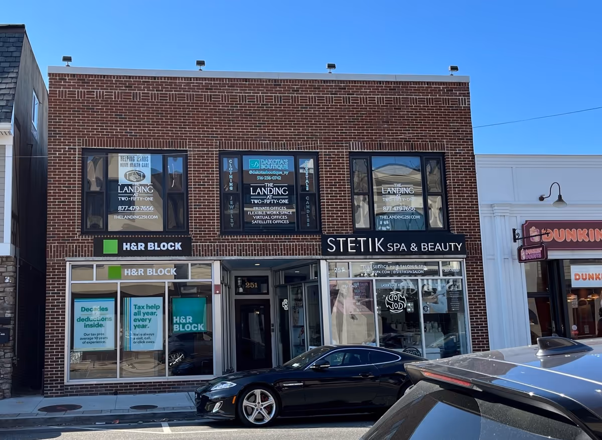 Brick storefront building with H&R Block and STETIK Spa & Beauty signage, parked cars along street.