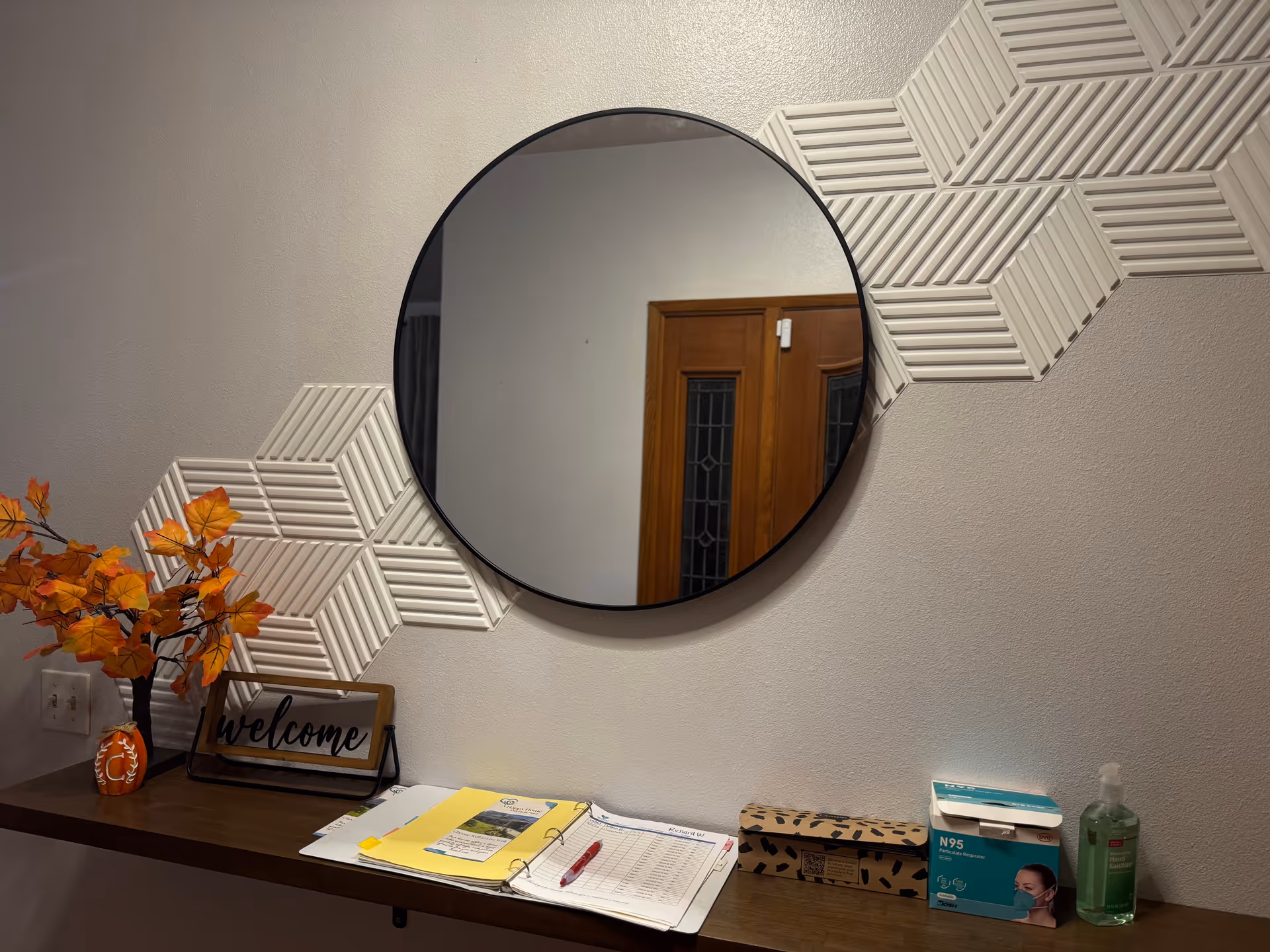 Round mirror above a desk with a welcome sign, autumn leaves, and supplies.