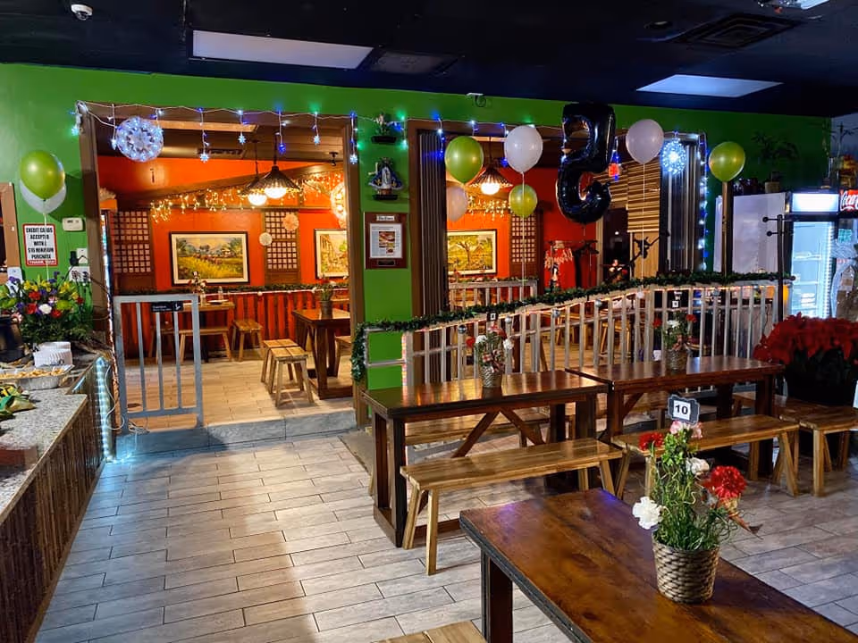 Festive dining area with long wooden benches, balloons, and string lights inside a senior facility