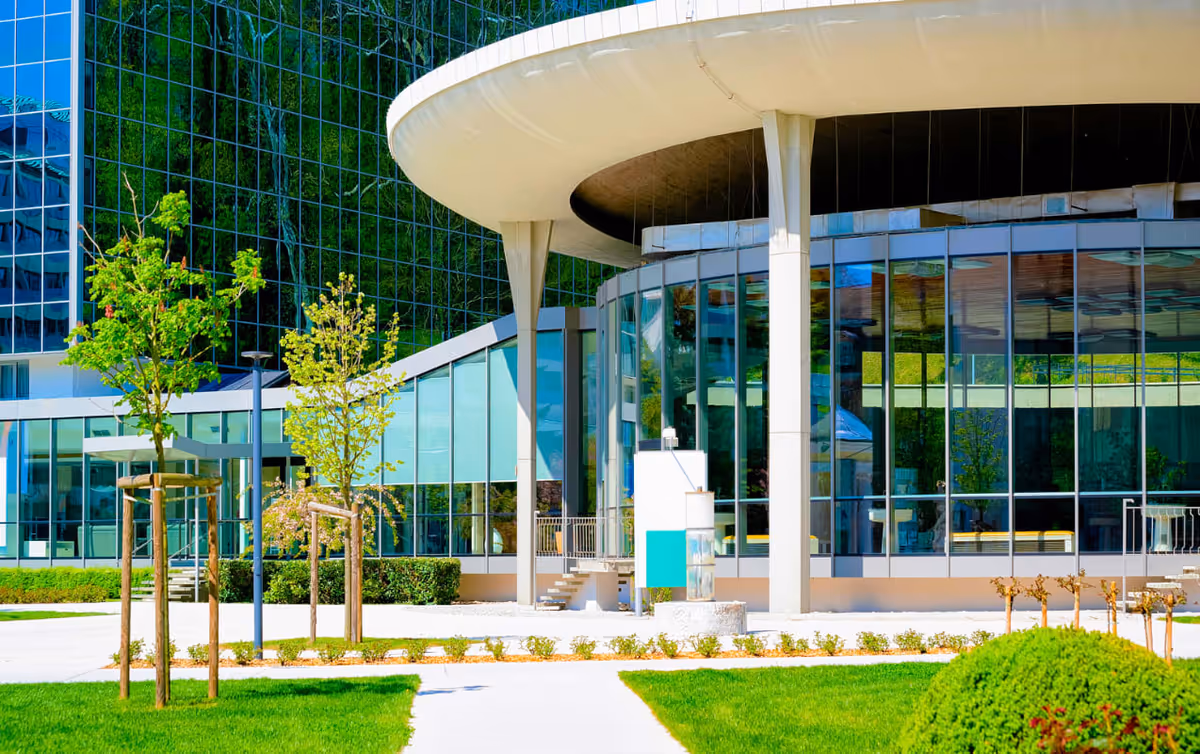 Modern glass-front facility with curved canopy and manicured lawn on sunny day.