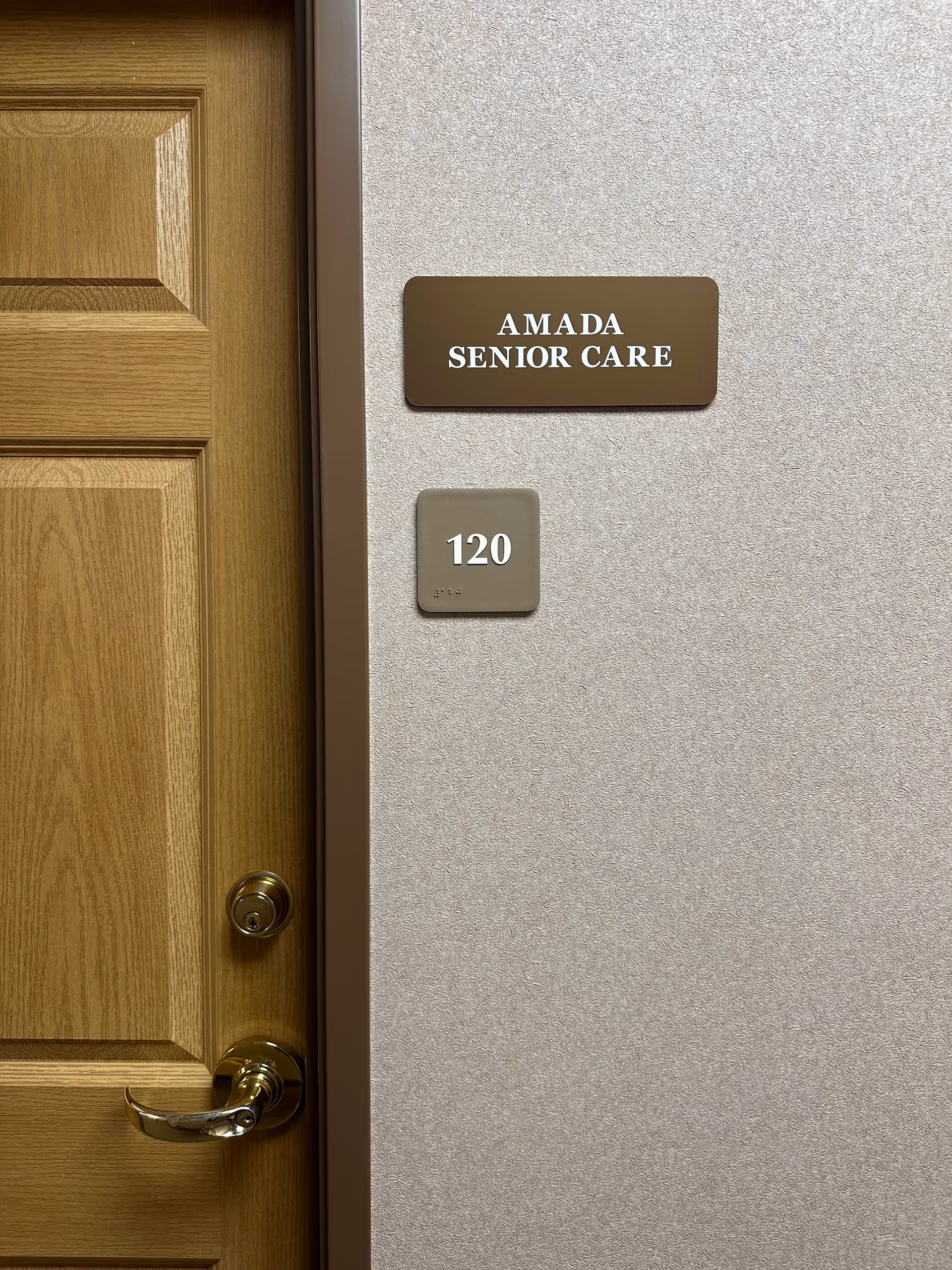 Wooden door with Amada Senior Care plaque and suite number 120 on wall