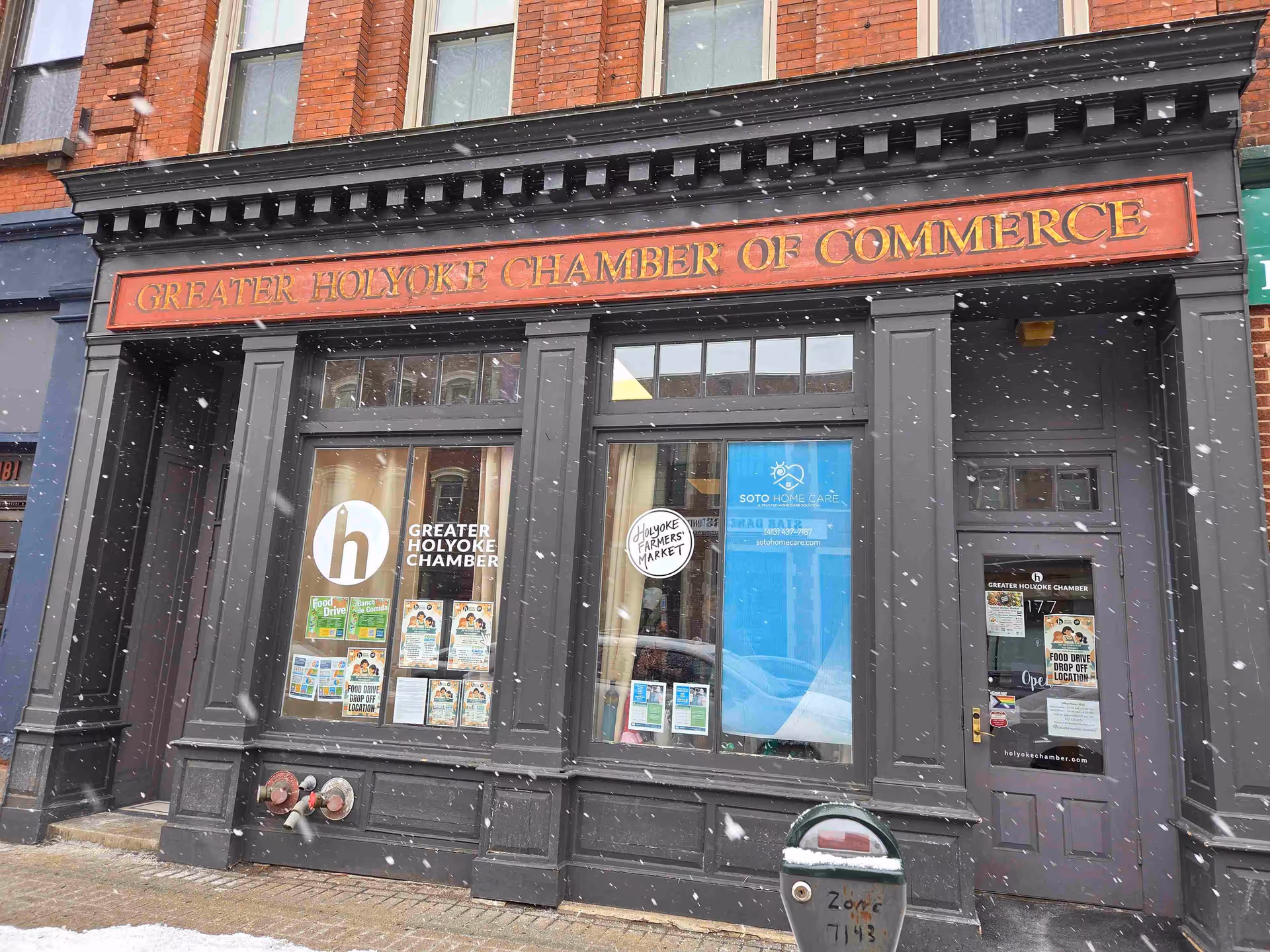 Brick storefront exterior with Greater Holyoke Chamber of Commerce sign, posters, and snowfall.
