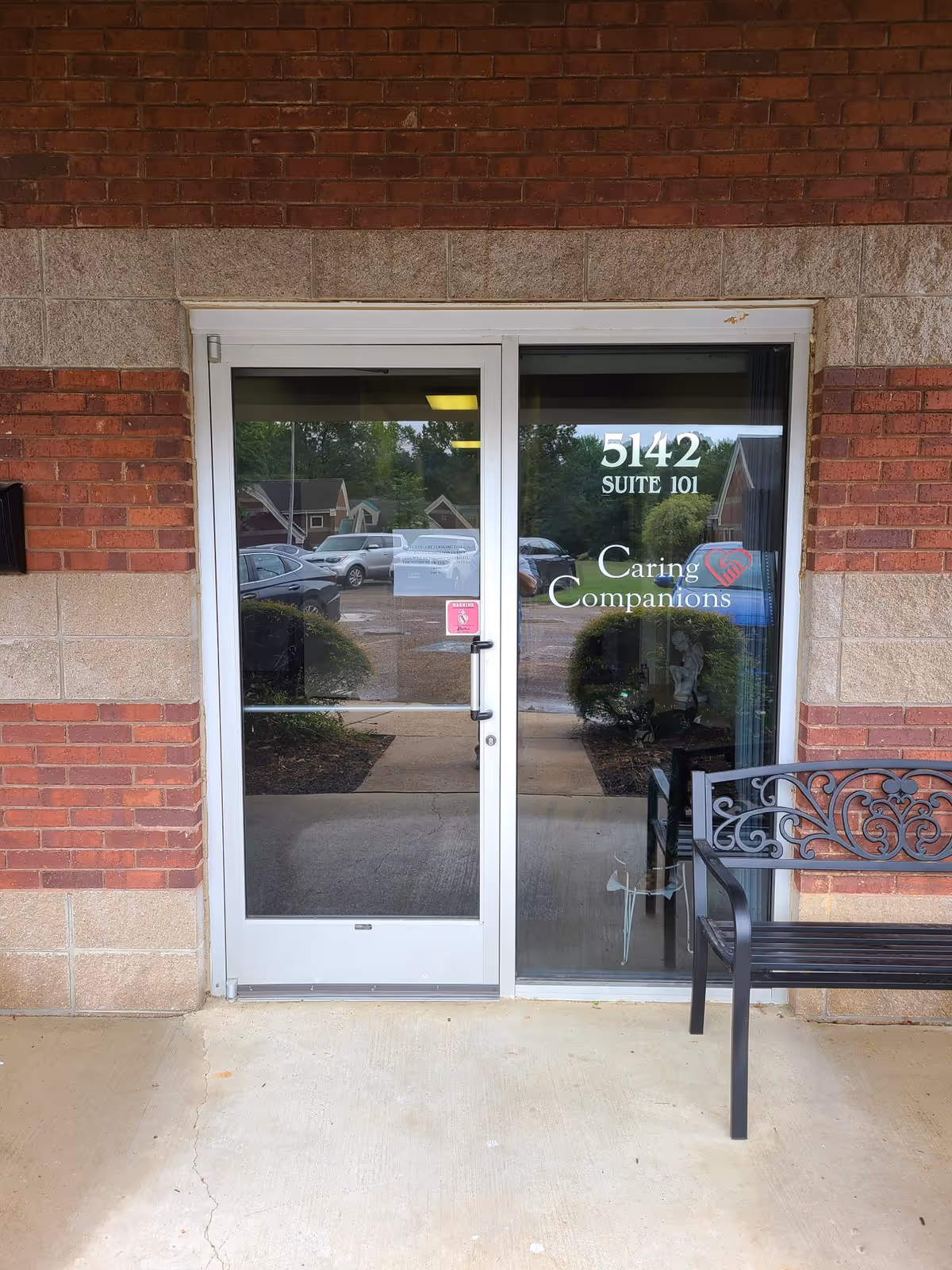 Glass doors of Caring Companions entrance with brick exterior and bench nearby.