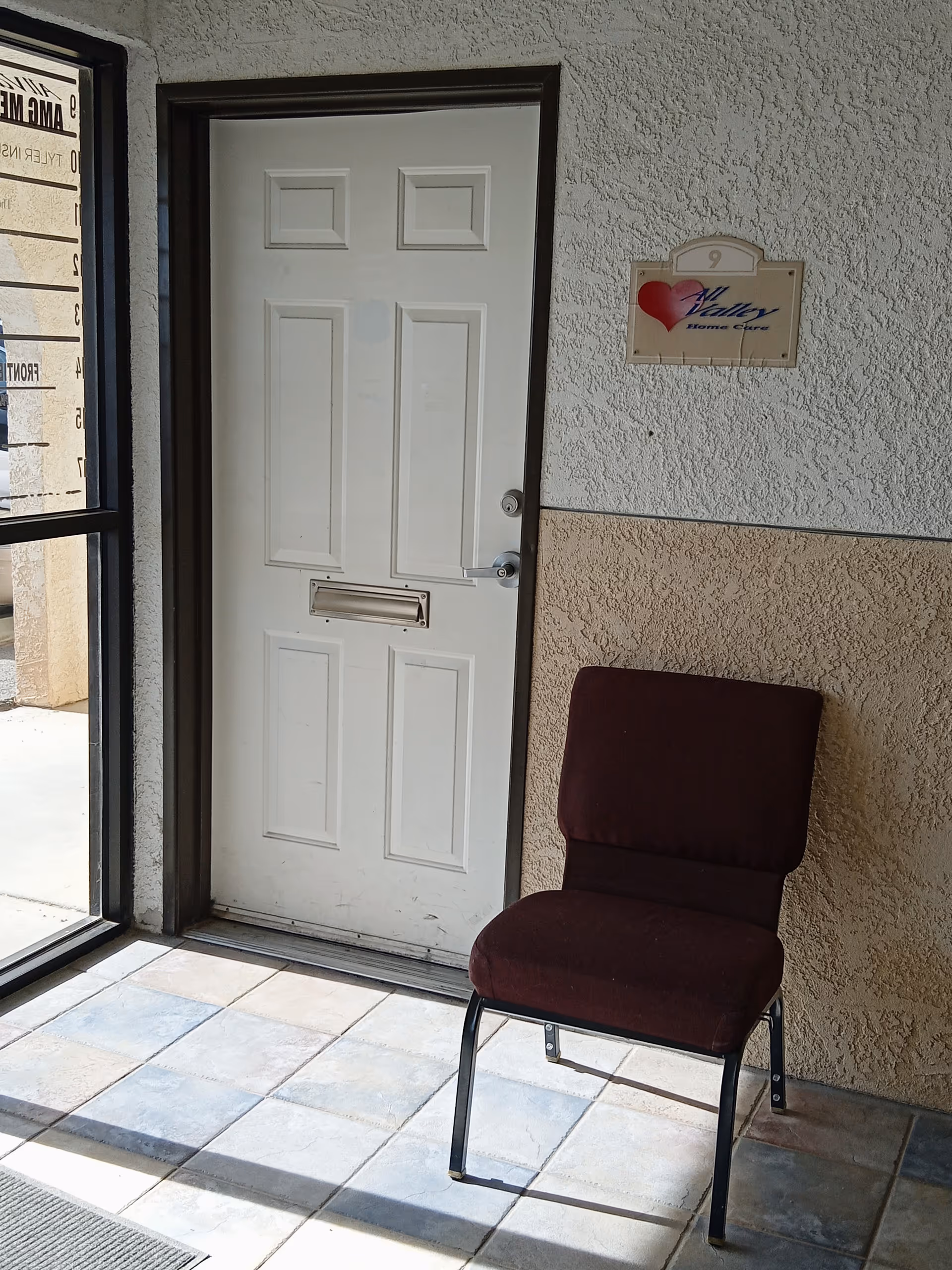 Entrance area with a white door, plaque, and a maroon chair against a textured wall.