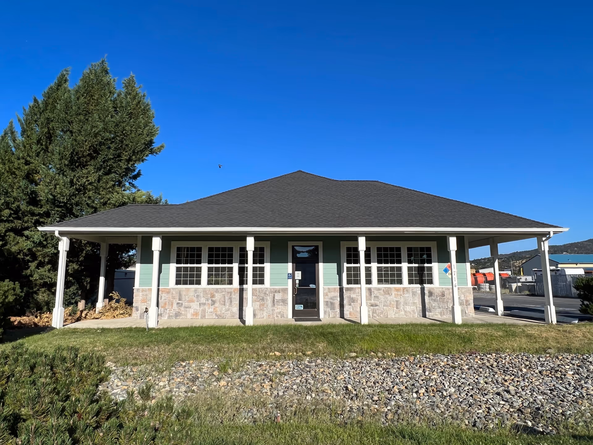 Single-story building with a covered front porch, stone facade, and clear blue sky.