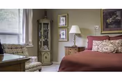 A cozy bedroom with a red bedspread, lamp, and seating near a window.