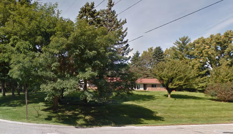 Front lawn with trees and a single low building, Chateau of Bloomfield, under a clear sky.