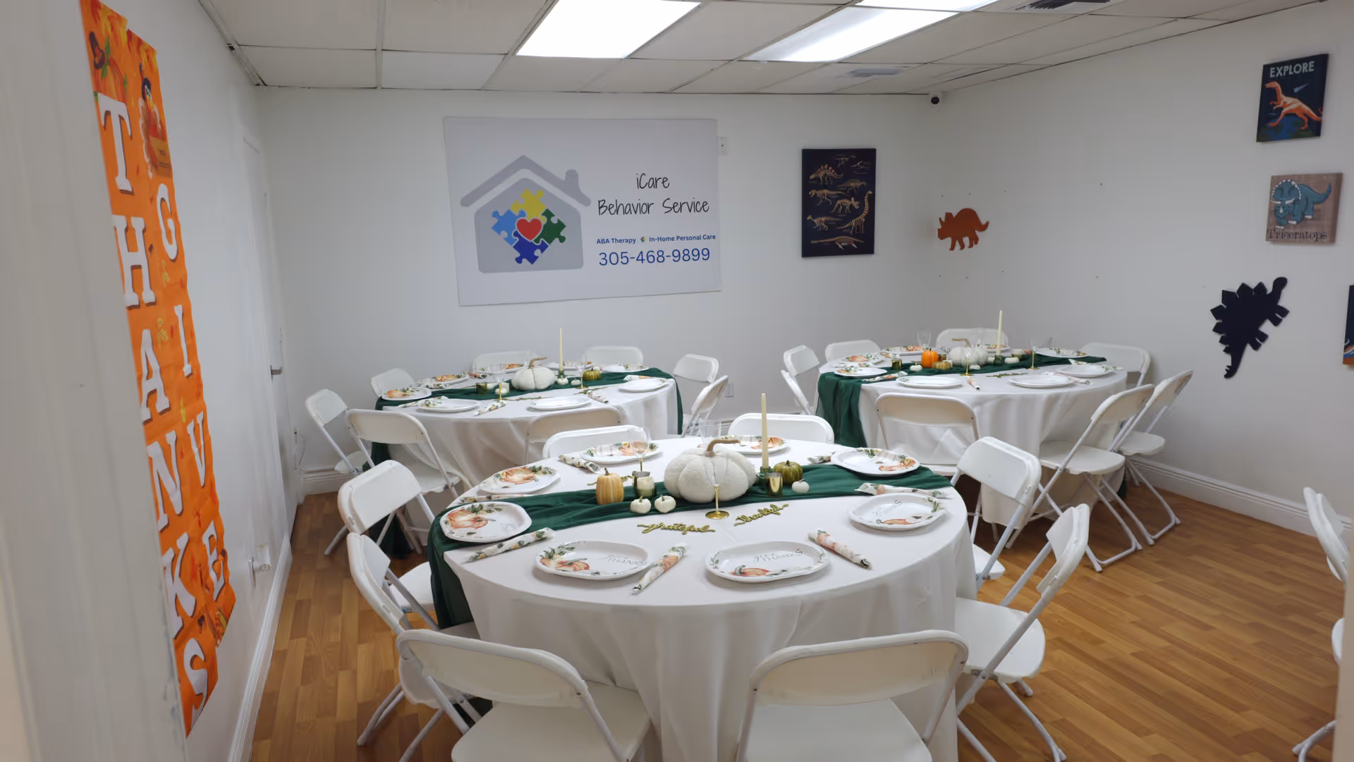 Round tables with white tablecloths and chairs arranged for a meal in a bright dining room.