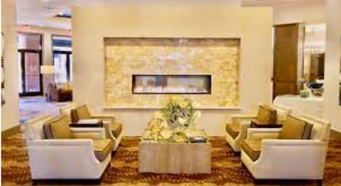 A cozy seating area with four armchairs around a coffee table facing a wall-mounted linear fireplace in a well-lit lounge.