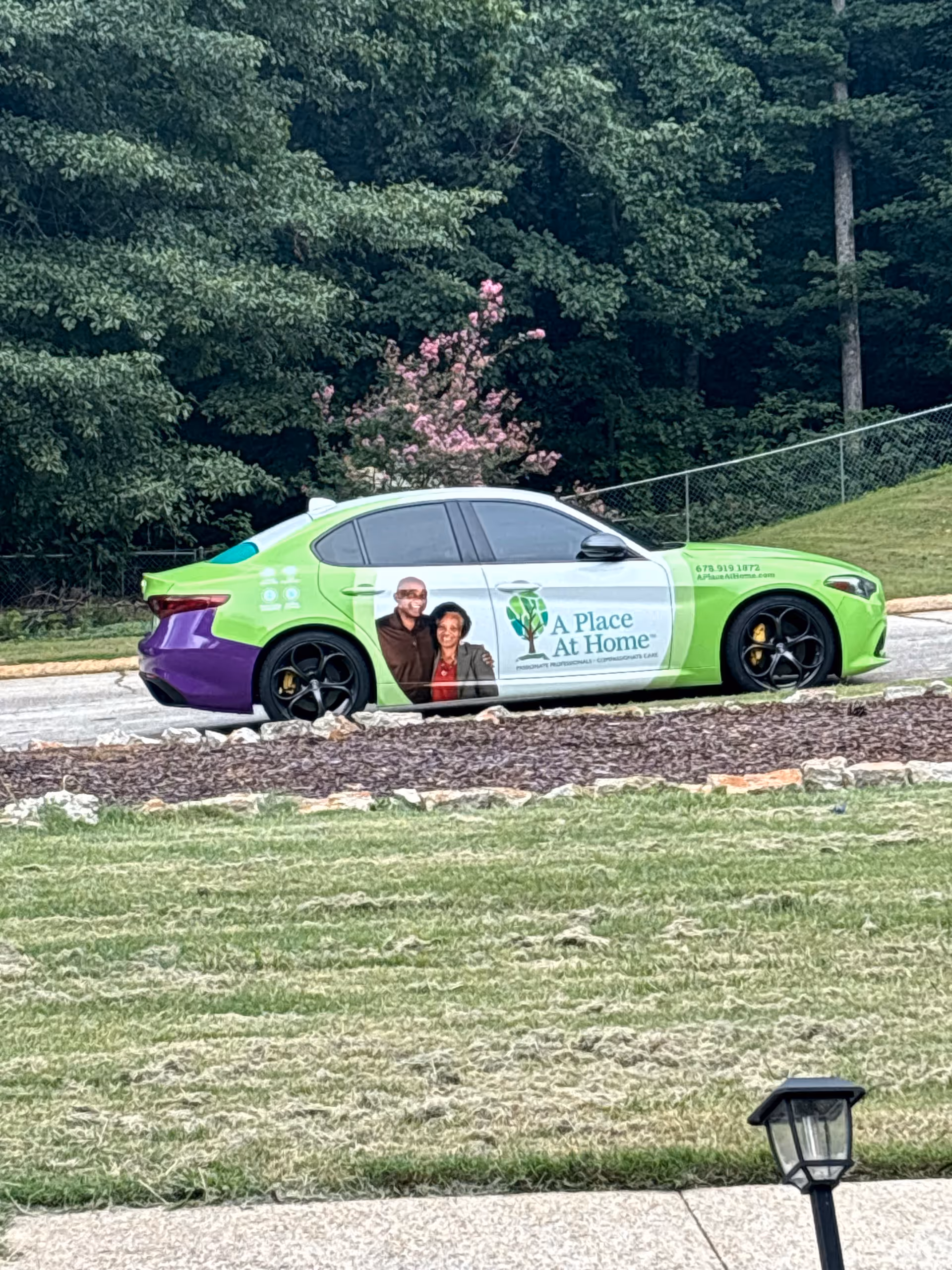 Colorful promotional car for A Place At Home Alpharetta parked outdoors beside trees.