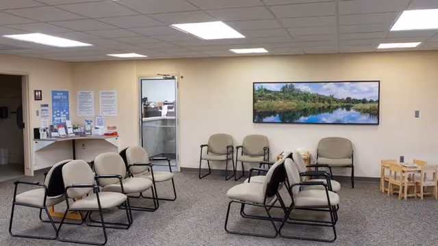 Waiting area with beige chairs arranged in rows and a landscape photo on the wall.
