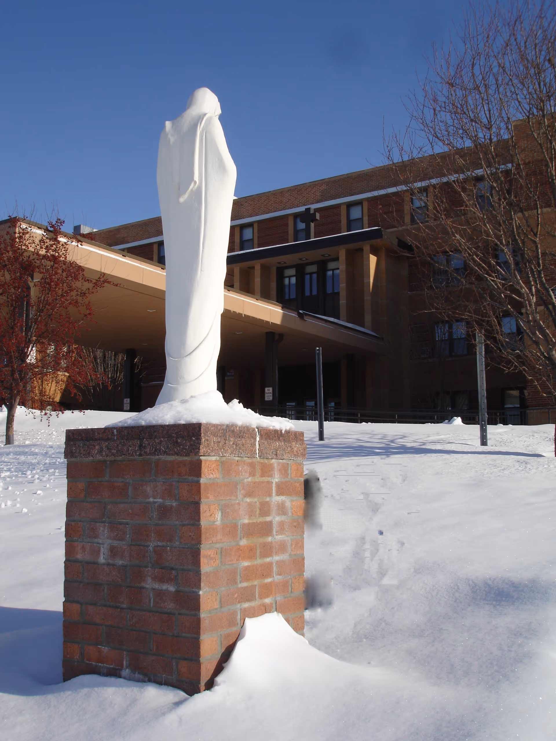 Snow-covered statue atop brick pedestal outside Benedictine Living Community-Crookston.