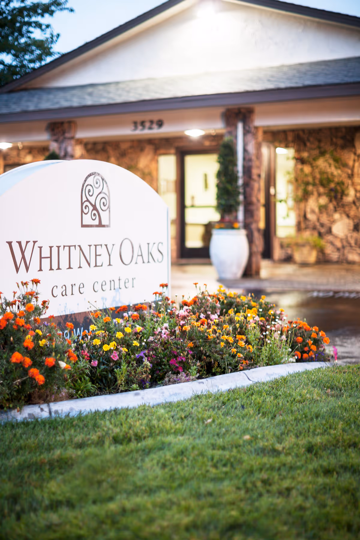 Whitney Oaks Care Center sign with colorful flowers and building entrance.