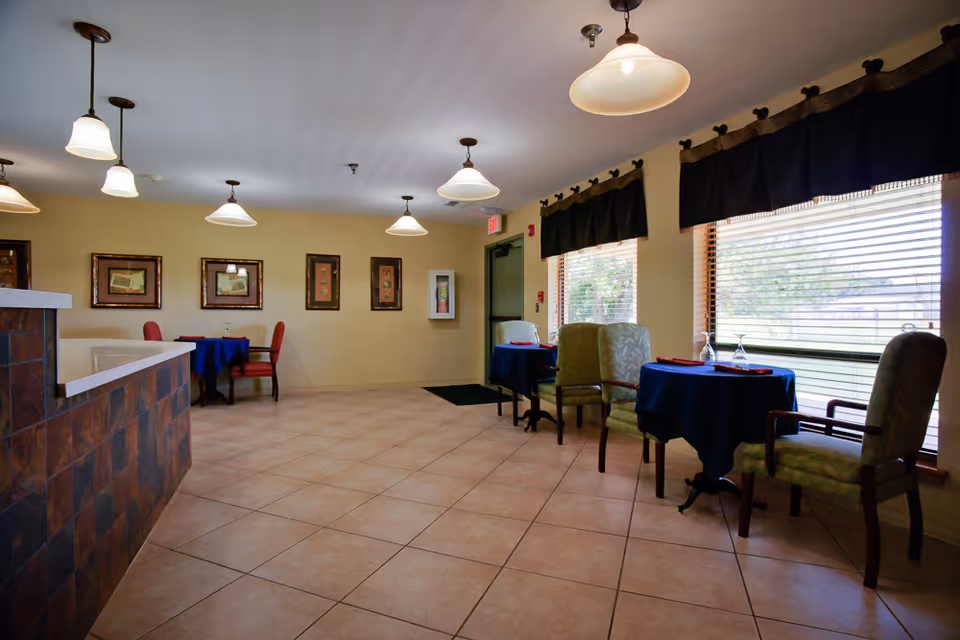 Dining area with tables, chairs, and large windows in a senior living center.