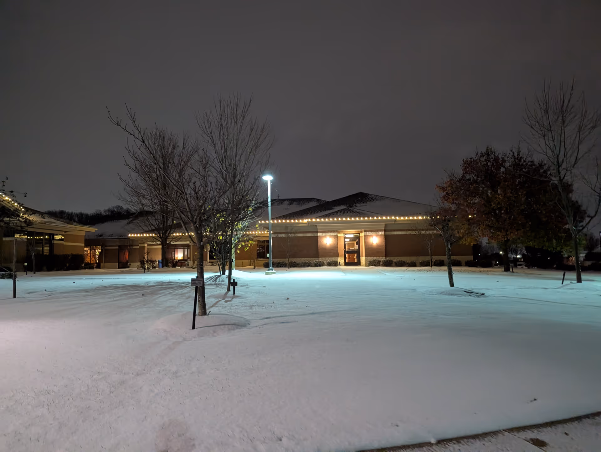 Night exterior of a hospice building with snow-covered ground and a lit entrance.