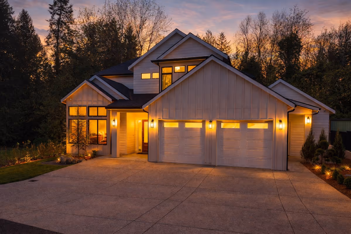 Exterior view of a modern house with a lit three-car garage at dusk.