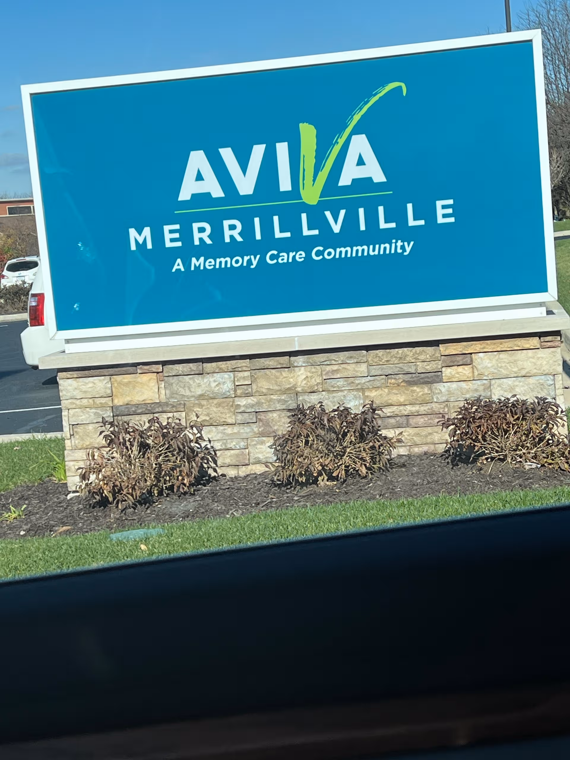 A blue AVIVA Merrillville sign with a stone base and shrubs in front.