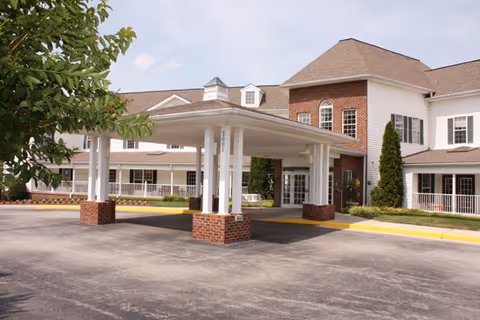 Front entrance of the Brookdale Salem senior living building featuring a white covered porte-cochère with brick columns and a brick-and-siding facade.