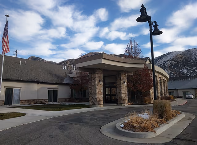 Front exterior view of a senior living facility entrance with stone columns and flag