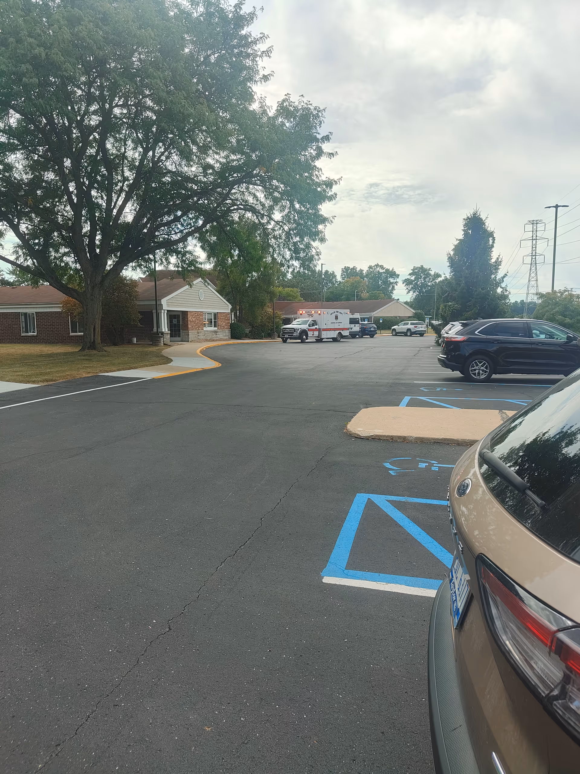 Exterior view of a senior living facility front with parking lot and vehicles.