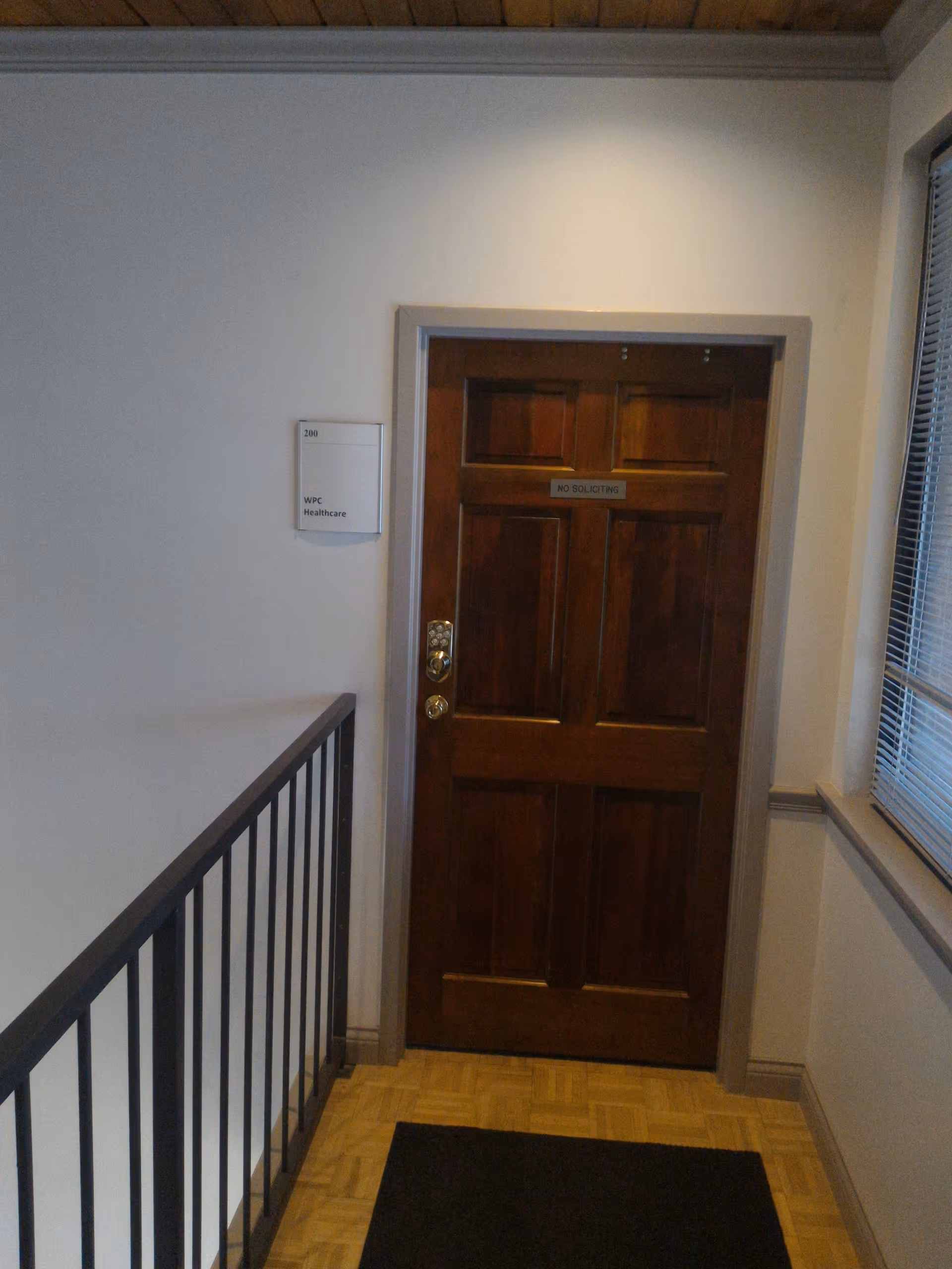 Interior hallway with a wooden door labeled No Soliciting, railing, and window blinds.