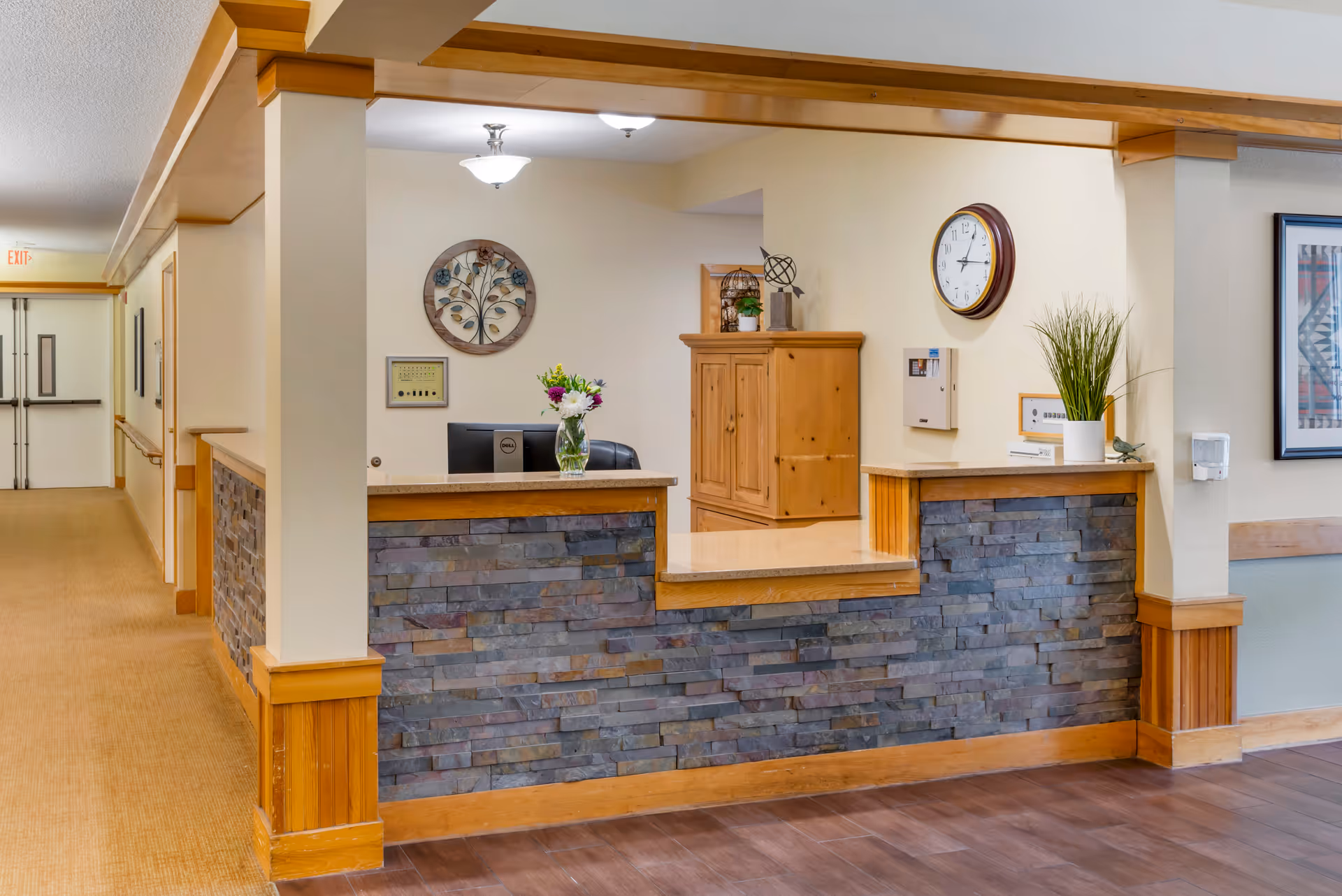 Reception desk with stone façade inside Brookdale El Camino, featuring hallway and clock.