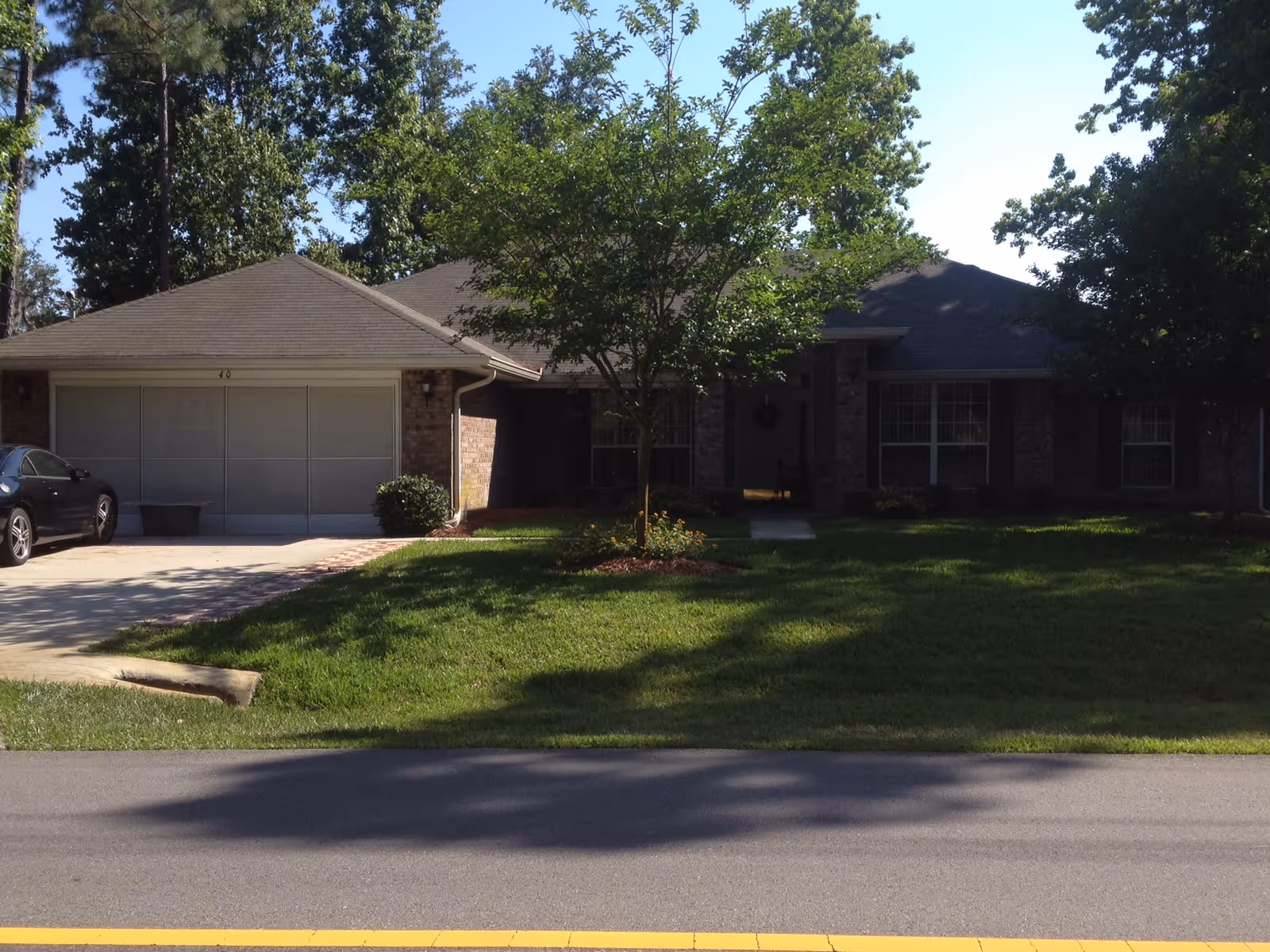 Single-story brick senior living facility with front lawn, trees, and a double garage.