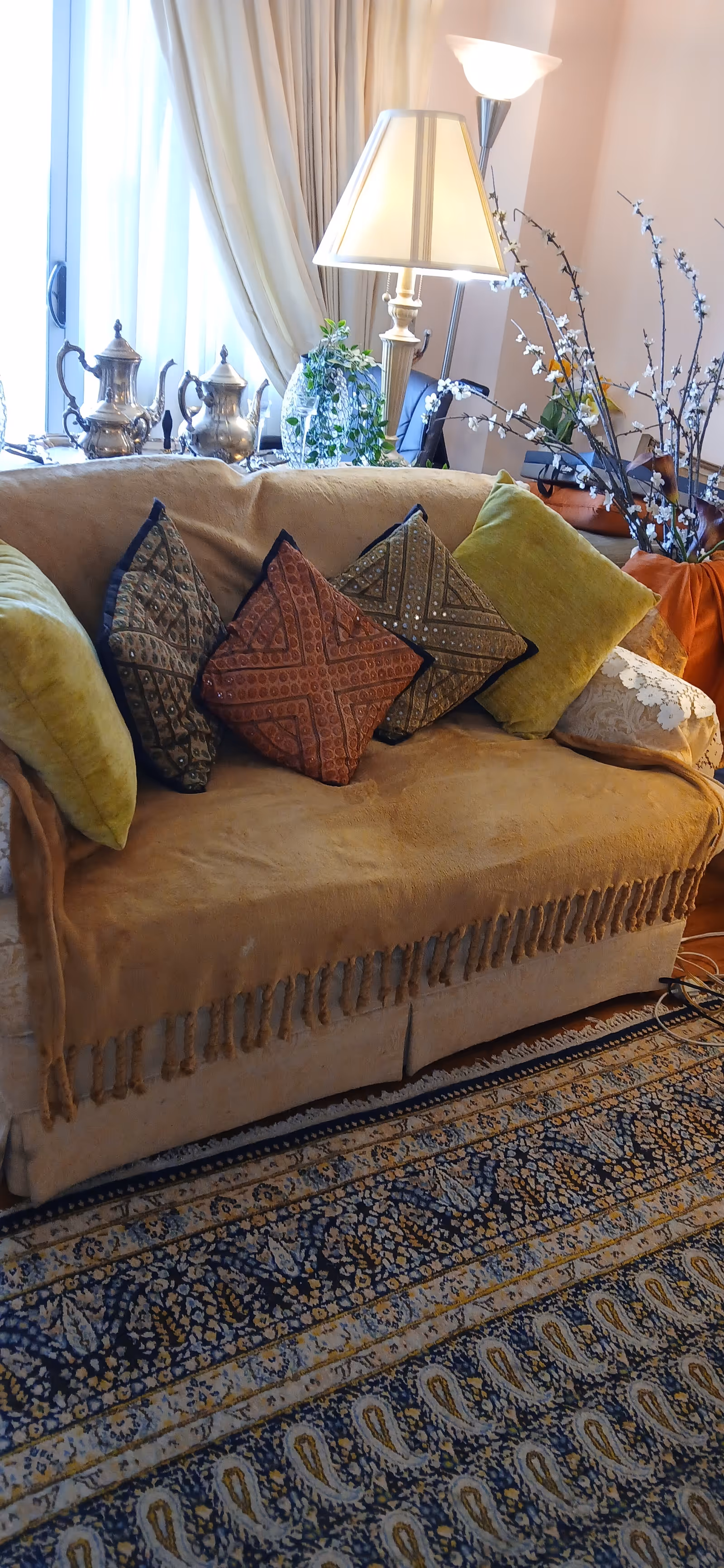 Beige sofa with colorful cushions, lamp, curtains, and patterned rug in cozy living room.