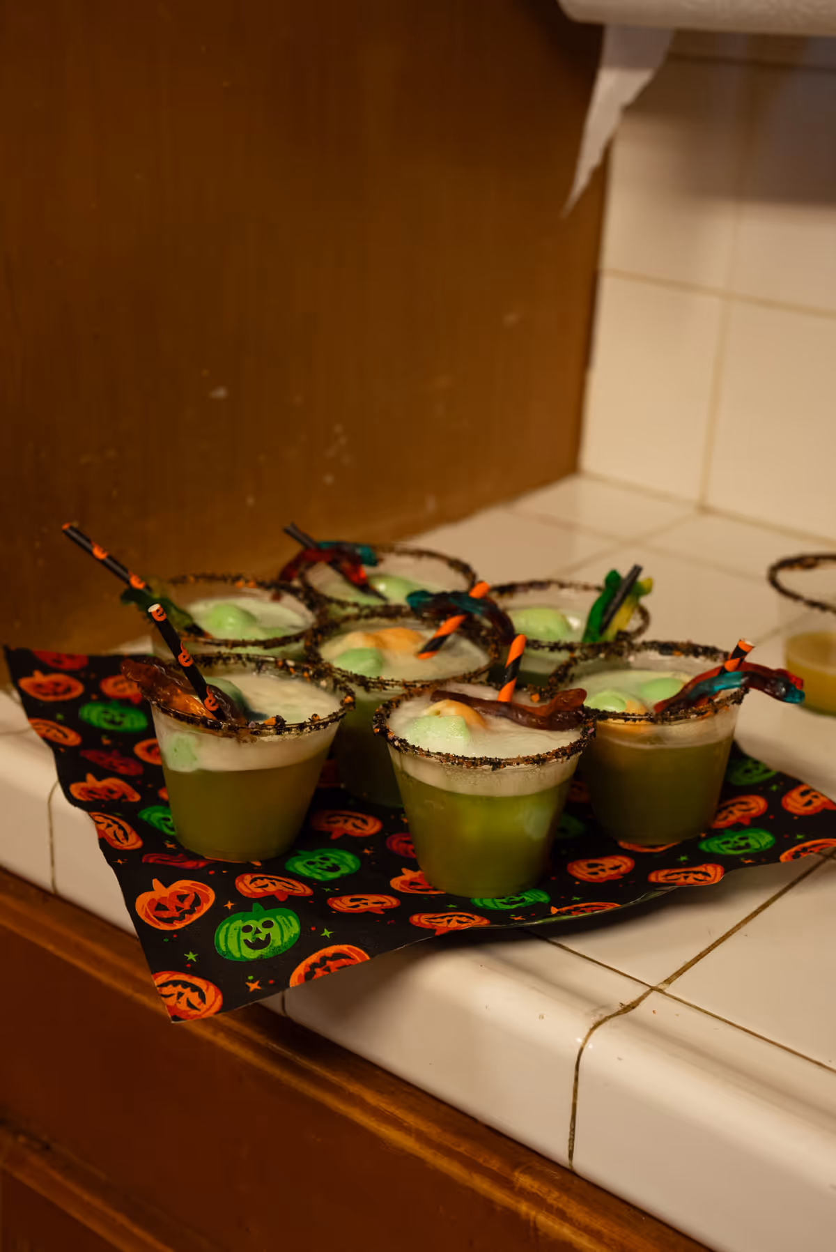 Several green Halloween drinks with salt-rimmed glasses on a pumpkin-patterned napkin.