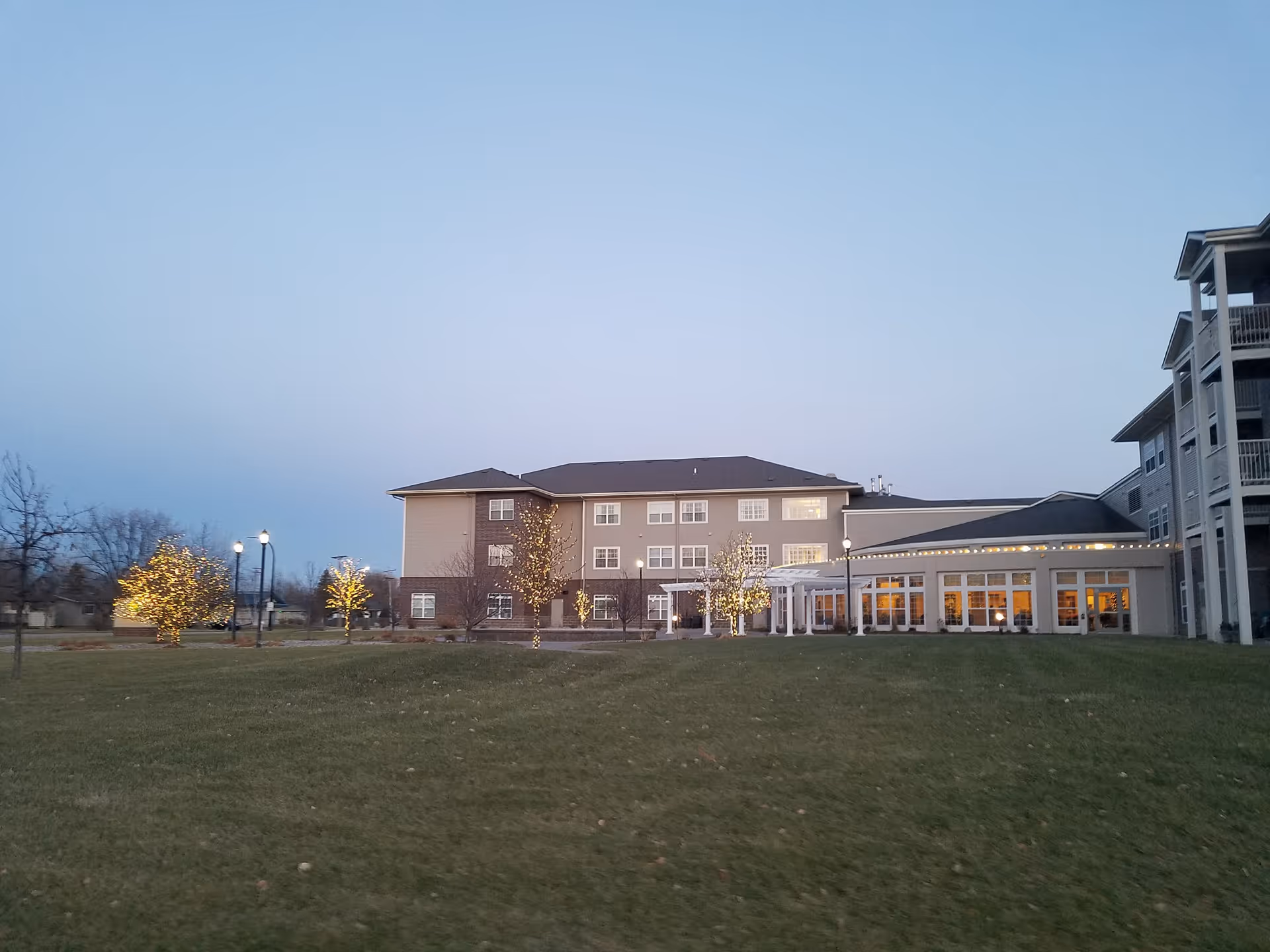 Exterior view of Eventide at Sheyenne Crossings with lit trees and a glass-front entrance.