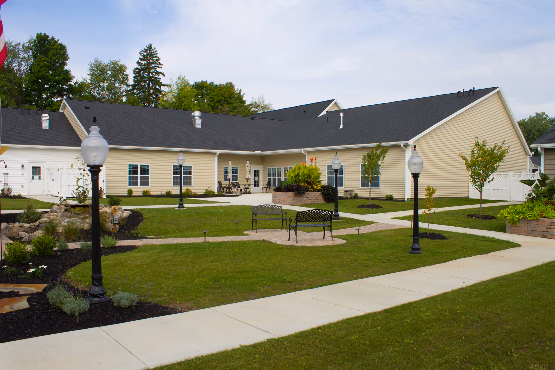 Exterior view of a single-story senior living facility with lawn and benches.