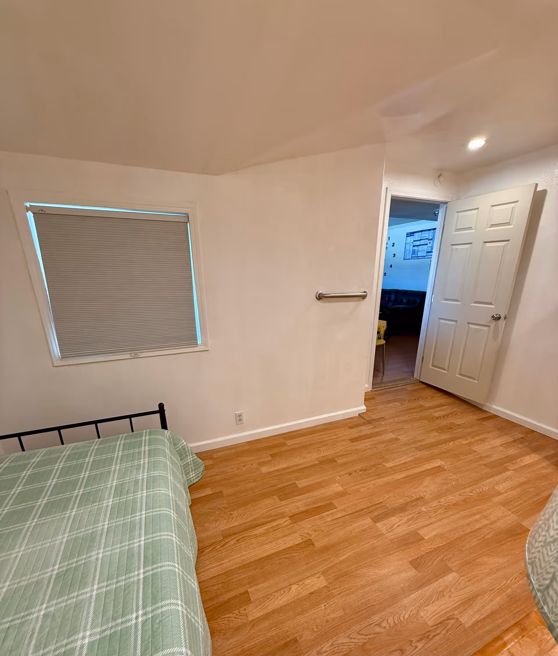 A small bedroom with a metal bed, window blinds, and a doorway to another room.