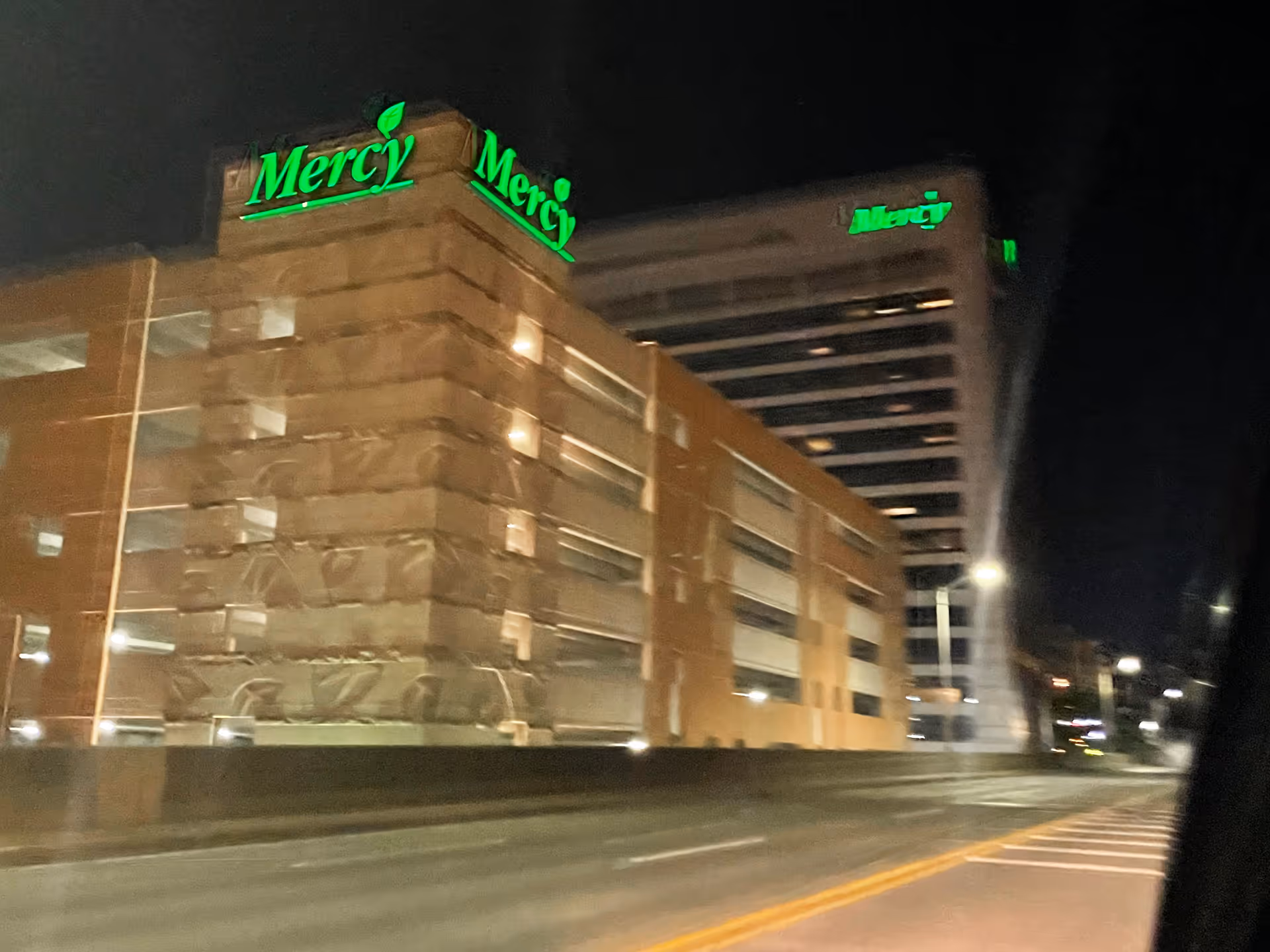 Nighttime exterior of Mercy Medical Center with green illuminated signage.