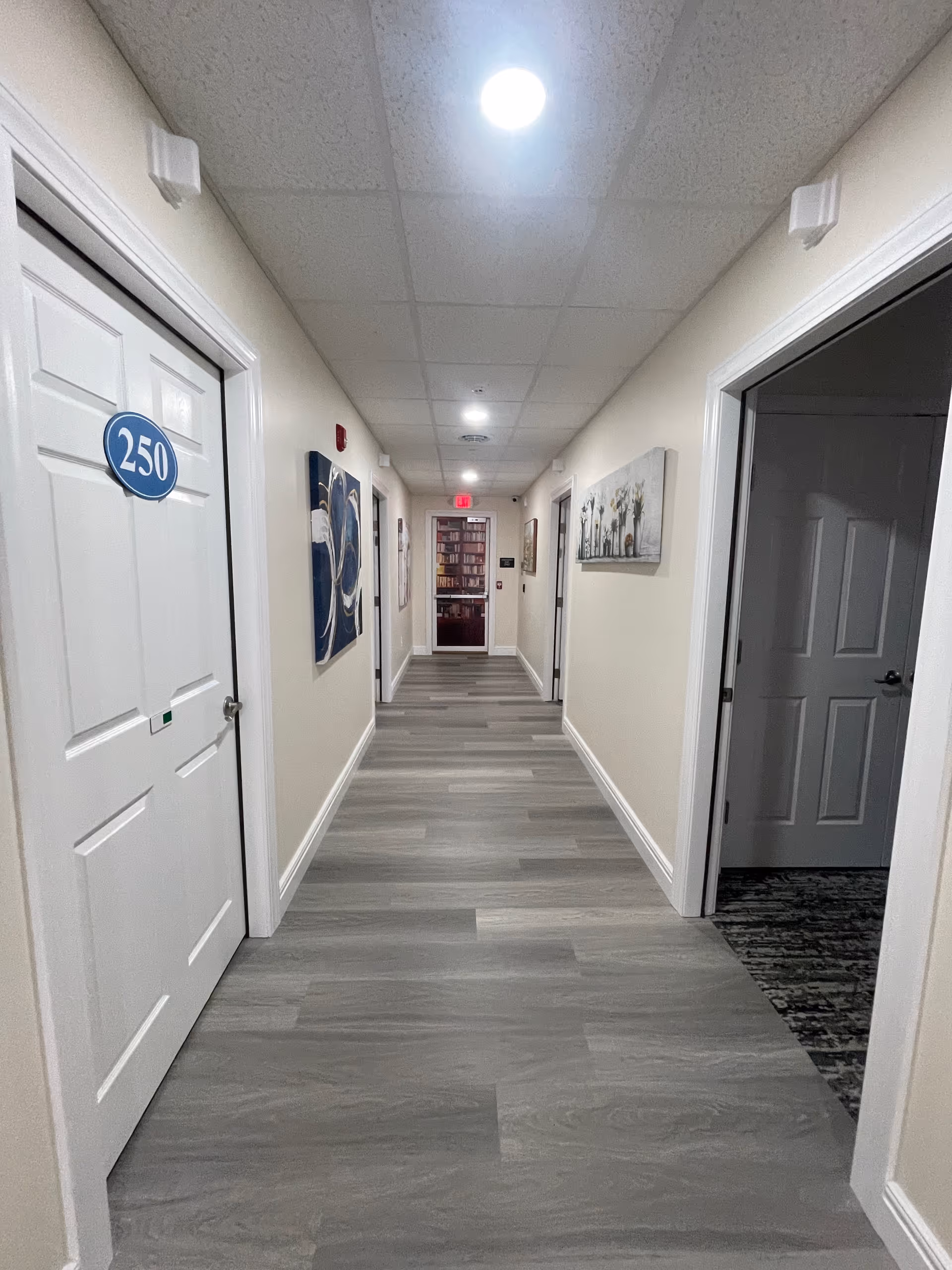 Long, well-lit hallway in a senior living facility with doors and wall art.
