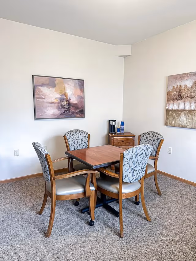 A small dining table with four upholstered chairs in a plain room.