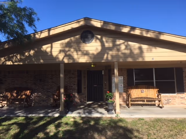 Front exterior of Kenedy Health & Rehabilitation, a single-story brick facility with a porch and benches.