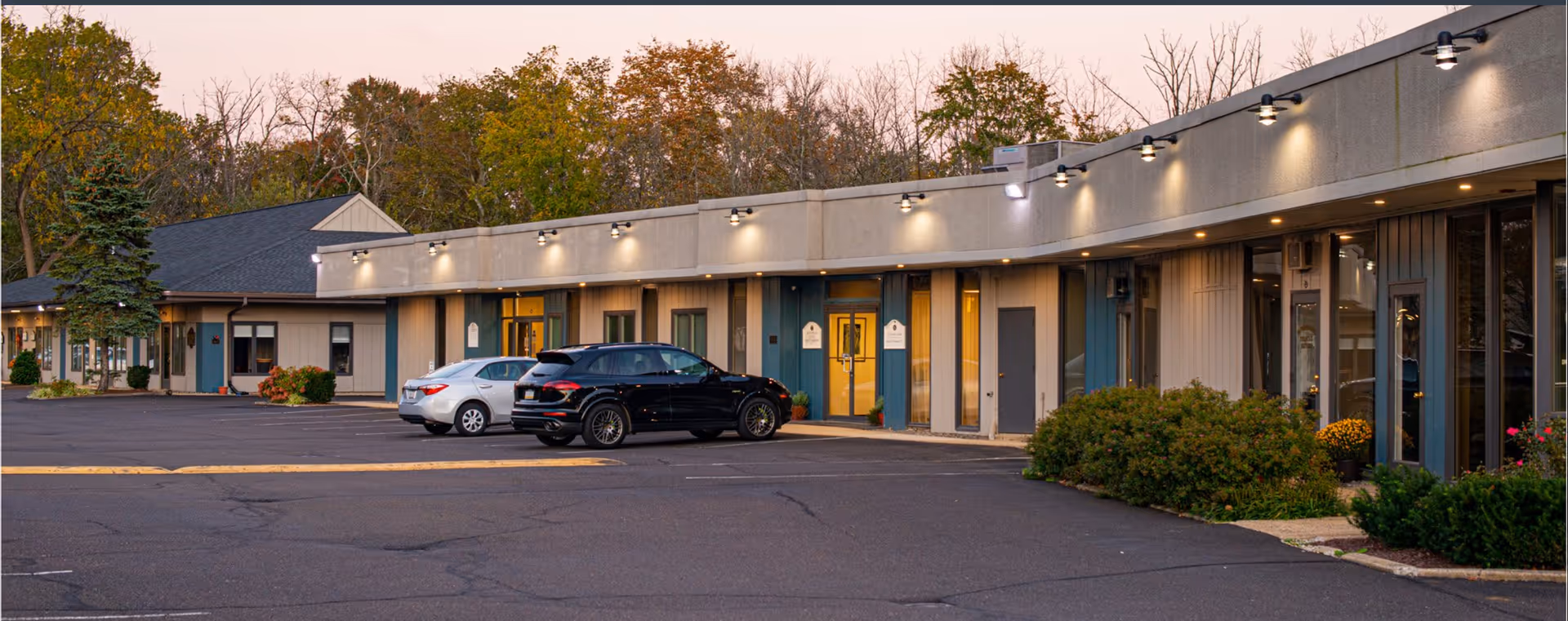 Exterior view of a single-story senior living facility with a parking lot and cars.