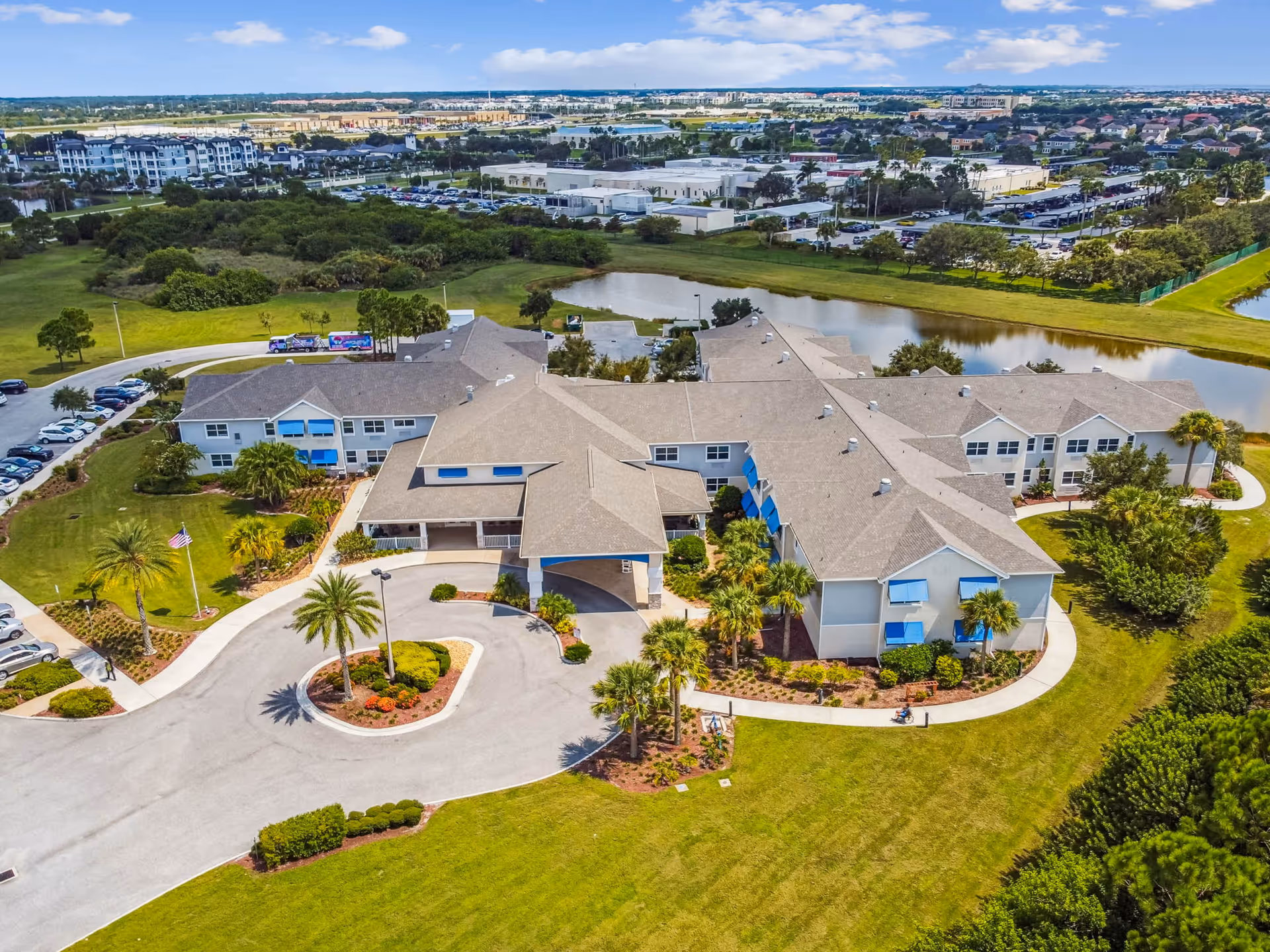 Aerial view of a large senior living campus with gray roofs, green lawns, and a pond