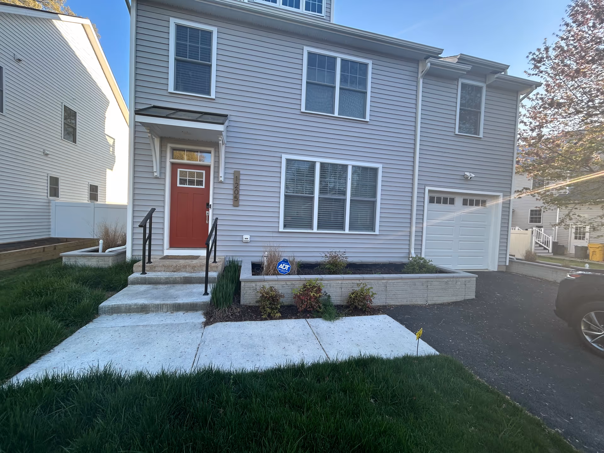 Two-story gray townhouse-style building with red front door, stairs, and driveway.